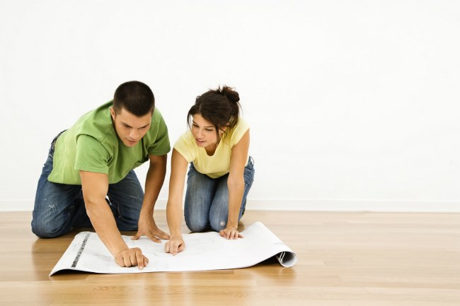 A man and woman on their hands and knees, looking at floor plans next to a wall