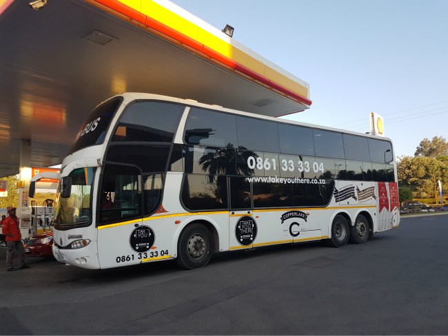 A black and white double-decker tour bus stationary at Shell garage